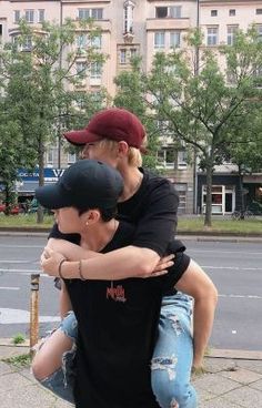 two people sitting on top of each other in front of a street with tall buildings