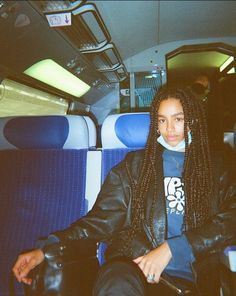 a woman with dreadlocks sitting on a bus looking off to the side, wearing a black leather jacket