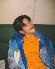 a young man sitting on top of a green couch next to a white wall and wearing an orange shirt