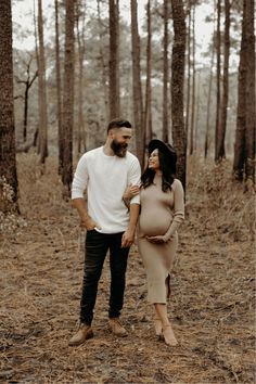 a pregnant woman standing next to a man in the woods