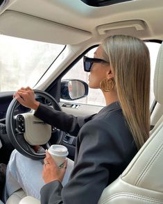 a woman sitting in the driver's seat of a car holding a coffee cup