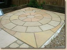 a stone patio with a circular design in the middle and a wooden fence behind it