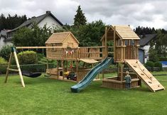 a wooden playset with a slide and climbing frame in the grass next to a house