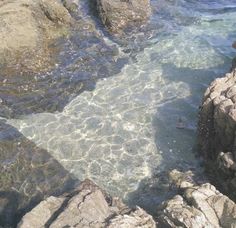 the water is crystal blue and clear at this rocky beach area with people swimming in it