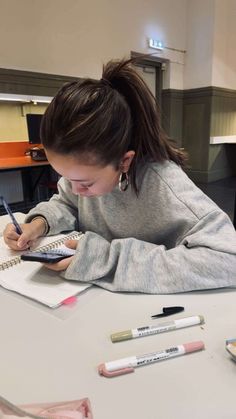 a woman sitting at a table writing on a piece of paper with crayons next to her