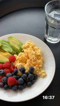 a white plate topped with eggs and fruit next to a glass of water on a table