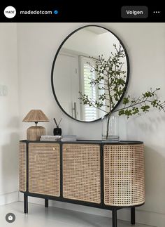 a large round mirror hanging on the wall above a wicker sideboard with drawers