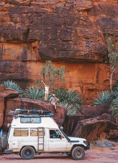 a white van parked in front of a mountain with people climbing on the side of it