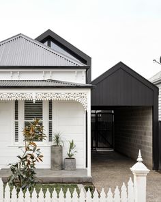 a white house with a black roof next to a white picket fence and two planters