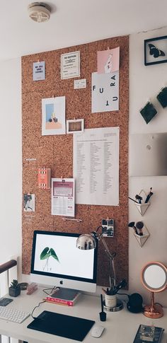 a desk with a computer on top of it in front of a cork board wall