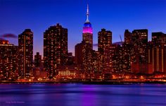 new york city skyline at night with the empire building lit up in purple and blue