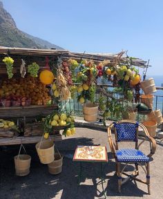 an outdoor fruit stand with lots of fruits hanging from it's roof and chairs