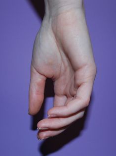 a person's hand holding something in the air on a purple background with only one finger visible