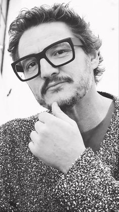 black and white photograph of a man with glasses looking at the camera while holding his hand to his chin