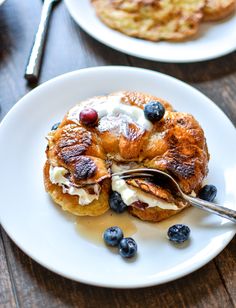 pancakes with blueberries and whipped cream are on a white plate next to silverware