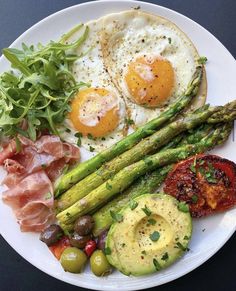 a white plate topped with asparagus, eggs and other food on top of it