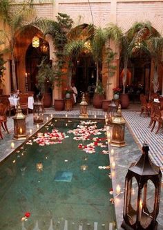 an indoor pool with candles and flowers on the water in front of some people sitting at tables