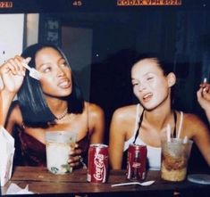 two young women sitting at a table with drinks and sodas in front of them