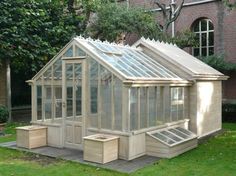 a small wooden greenhouse in the middle of a grassy area next to a brick building