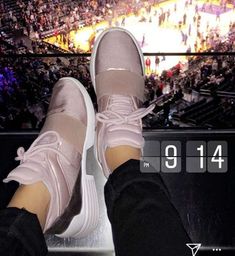 a person's feet in pink sneakers on top of a bench at a basketball game