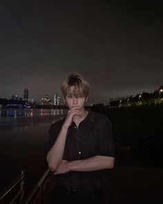 a young man is standing by the water at night with his hands on his chin