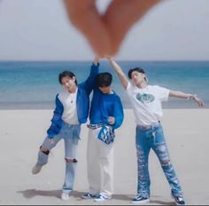 three young men standing on top of a beach next to the ocean holding their hands in the air