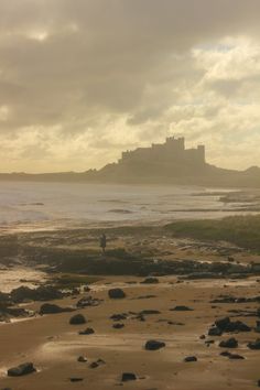 a person standing on top of a beach next to the ocean with a castle in the background