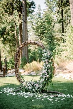 a wedding arch made out of branches with flowers and greenery on the ground in front of trees