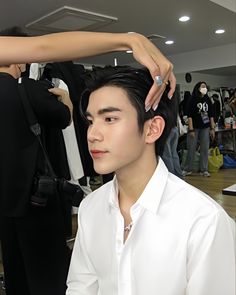 a man getting his hair cut by another person in a room full of other people