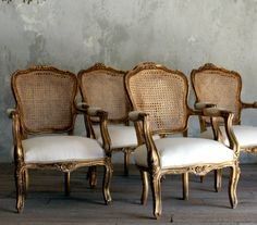 four antique chairs are lined up against a wall in an old fashion setting with white cushions