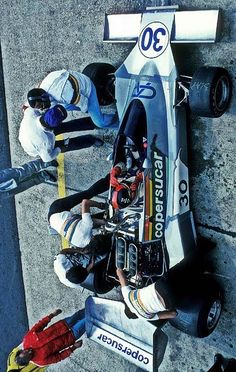 a man standing next to a racing car on top of a cement road near other people