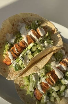 two tacos with chicken, lettuce and cucumber on them sitting on a plate