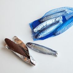 three fish wrapped in plastic sitting next to each other on a white counter top,