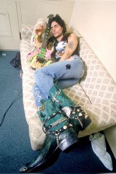 a man sitting on top of a bed next to a green bag and holding a guitar