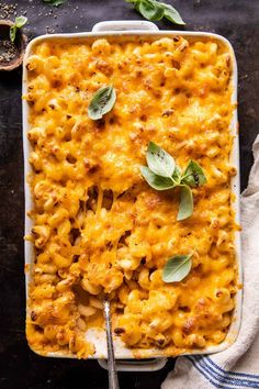 a casserole dish filled with macaroni and cheese topped with fresh basil