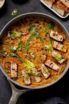 a pan filled with chicken and noodles on top of a black table next to other dishes