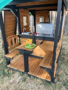 an outdoor kitchen made out of pallets and wooden planks in the grass with a green awning over it