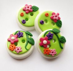 three green buttons with flowers on them sitting on a white surface, one is decorated in pink and purple