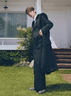 a young man in a suit and tie standing on the grass outside of a house