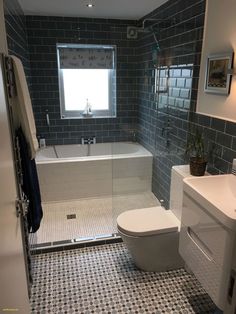 a white toilet sitting next to a bath tub in a bathroom under a window with blue tiles on the floor