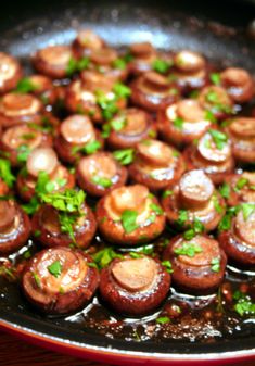 mushrooms are cooking in a frying pan on the stove with parsley sprinkled around them