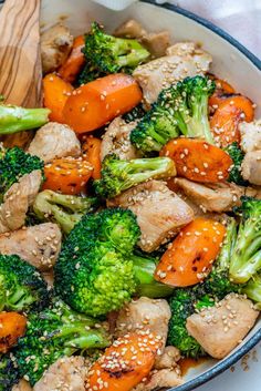 broccoli, carrots and chicken are mixed together in a bowl with sesame seeds