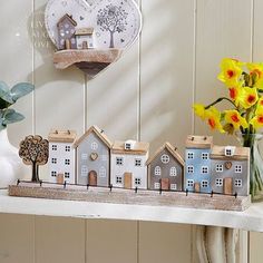 a white shelf topped with lots of small houses next to a vase filled with flowers