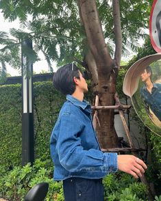 a man standing next to a tree with a mirror on it's face and his reflection in the mirror