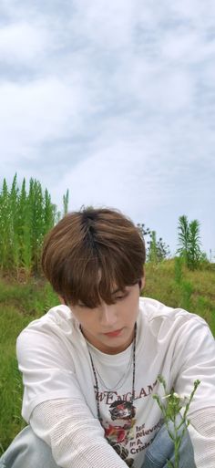 a boy sitting in the grass with his hands on his knees