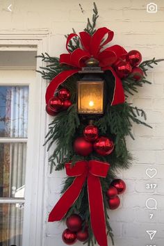 a christmas wreath hanging on the side of a white brick building with red ornaments and a lit candle