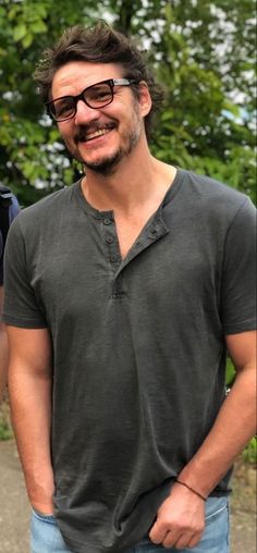 a man with glasses and a beard standing in front of some trees smiling at the camera