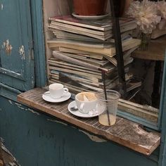 two cups and saucers on a window sill in front of a stack of books