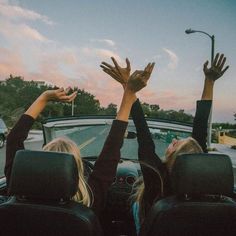 two women sitting in the back of a car with their hands up to the sky