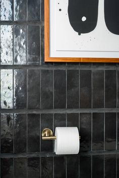 a bathroom with black tile and gold accents, toilet paper roll holder on the wall